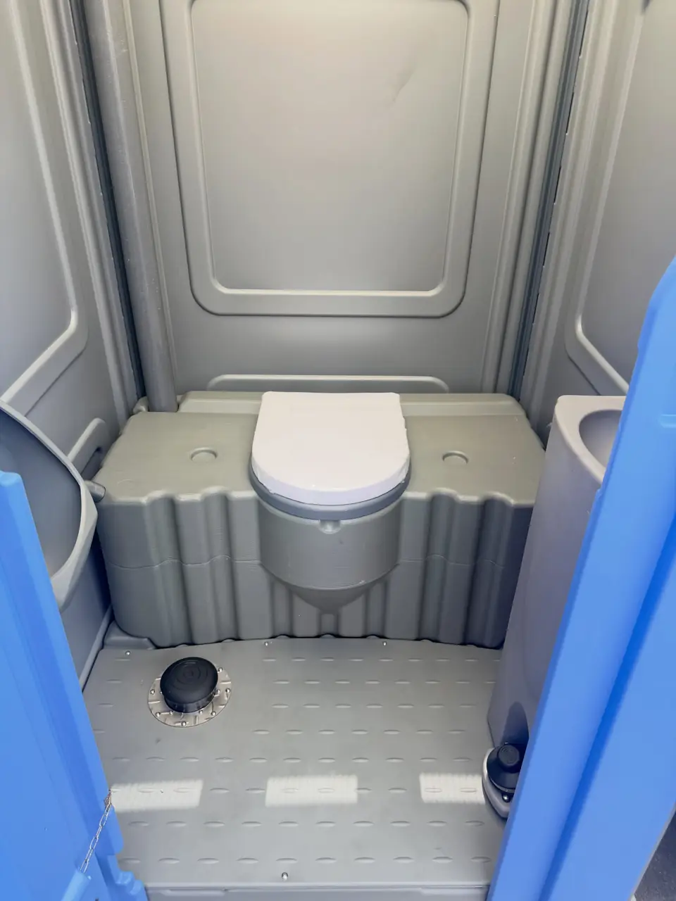 Inside a flushing portable toilet with gray molded floor and white seat