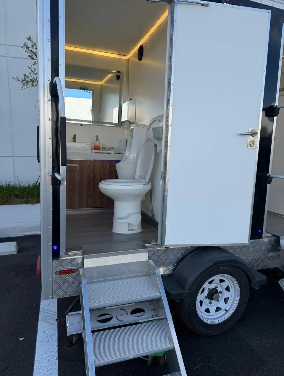Restroom trailer interior with porcelain toilet, wood vanity and lighted mirror