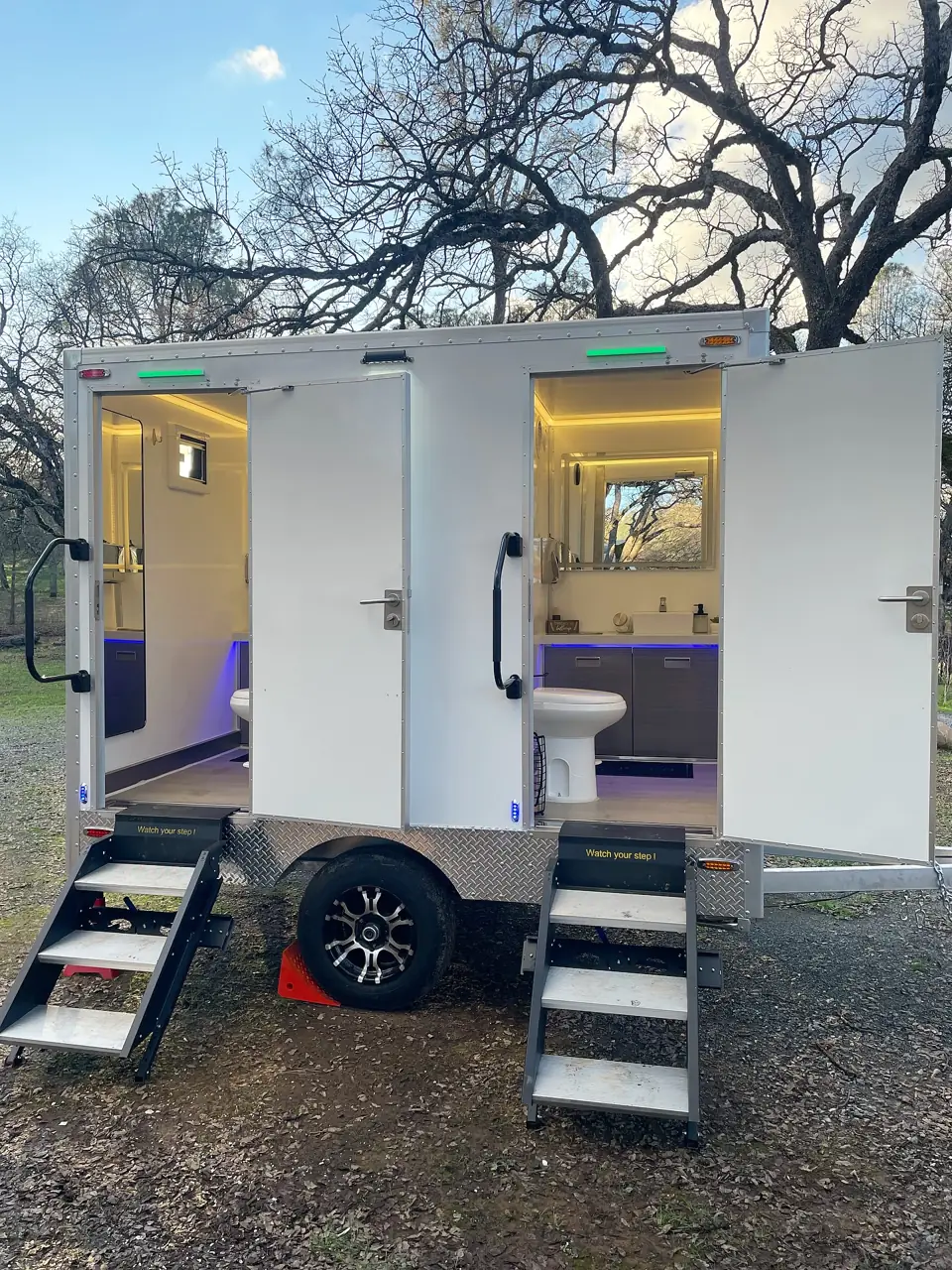 Two-stall restroom trailer with lit interiors, open doors and fold-down steps