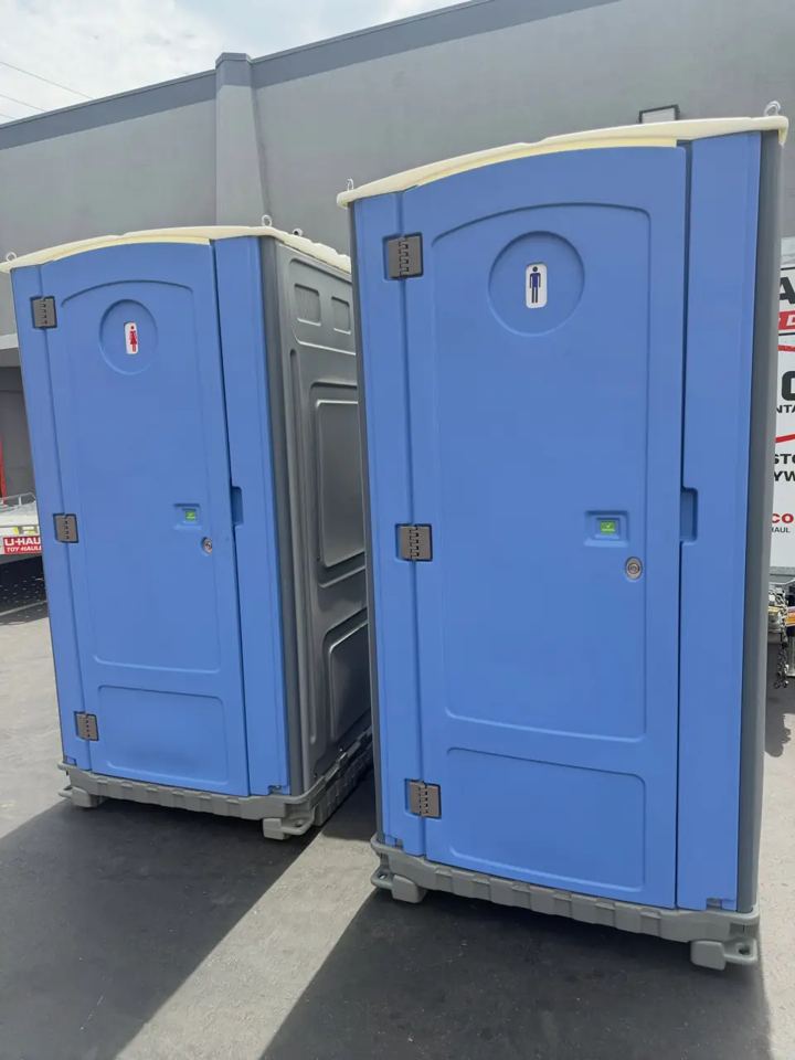 Two blue standard portable toilets parked side by side on pavement at a work site