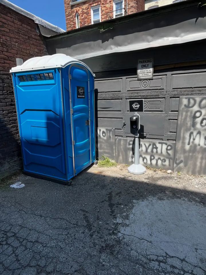 Single blue porta potty placed on a residential driveway next to a garage